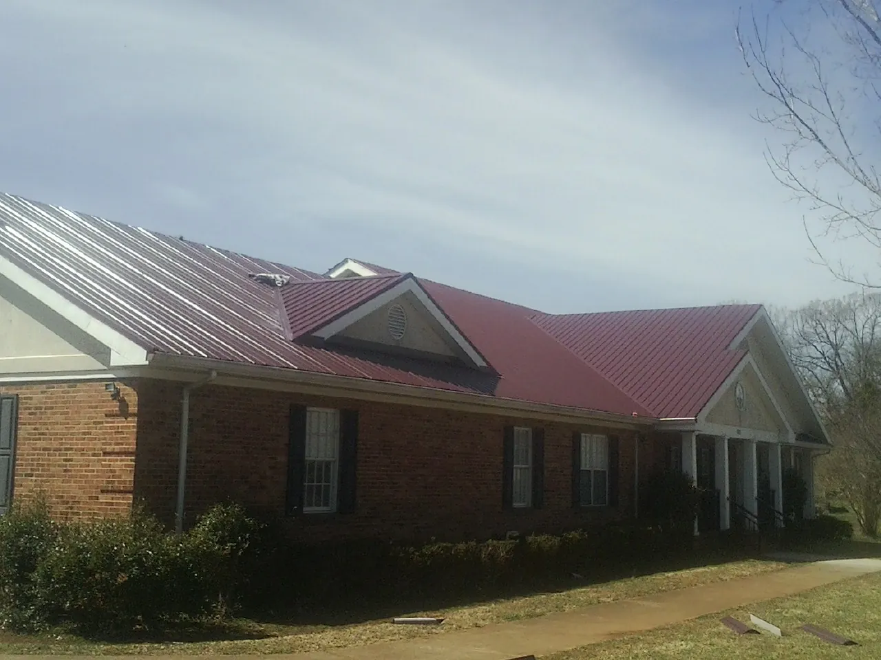 Red metal roof with gabled entries on a long brick building, from a Hail Damage Roof Repair job in Iron City