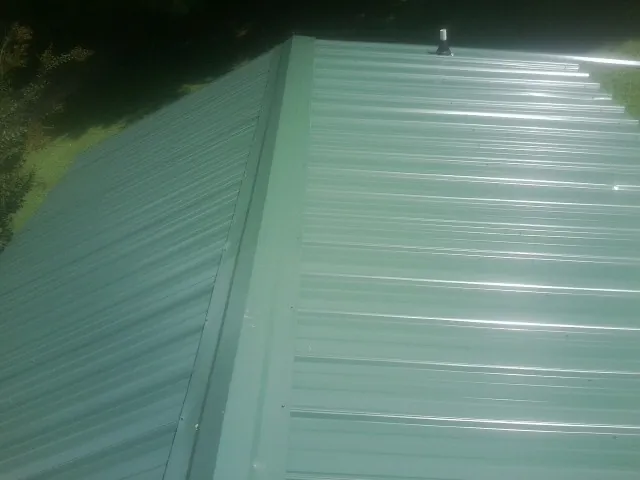 New green metal panels meeting at the ridge of a roof — Flat Roof Repair work by our crew in Iron City