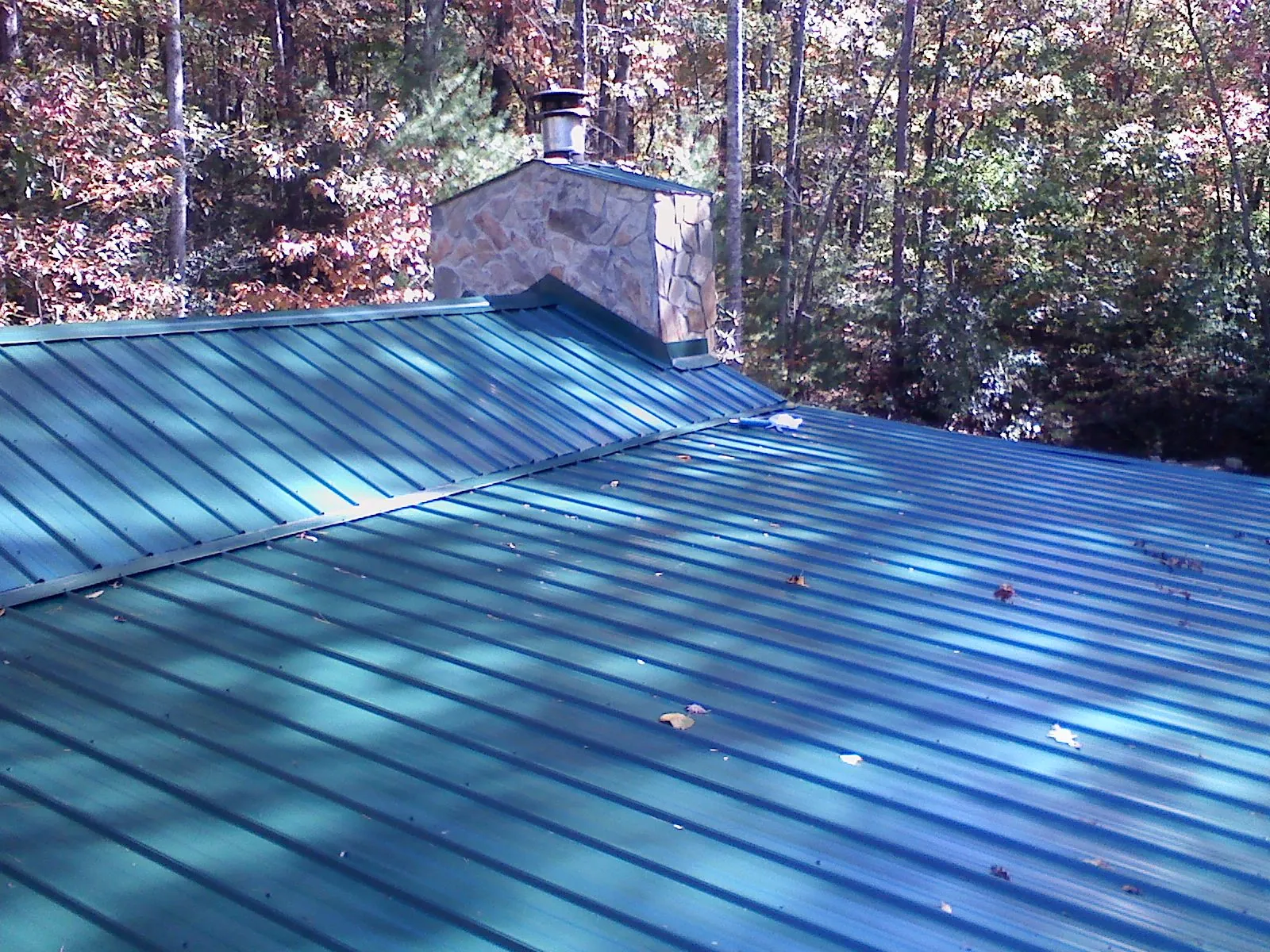 New green metal roof and stone chimney surrounded by autumn woods in Iron City