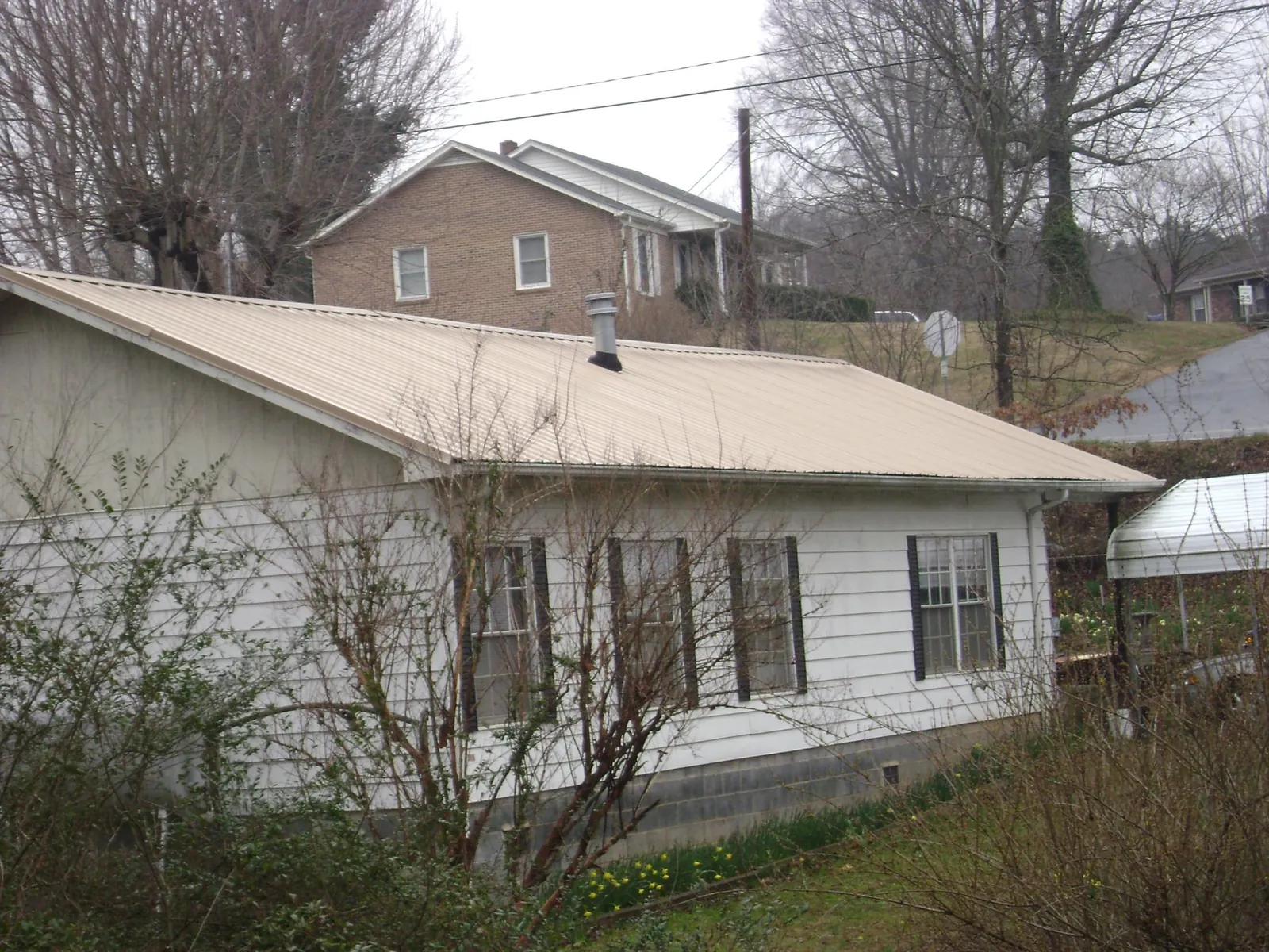 Tan metal roof on a white sided house set into a hillside — Commercial Roofing by Roofing Brothers in Iron City
